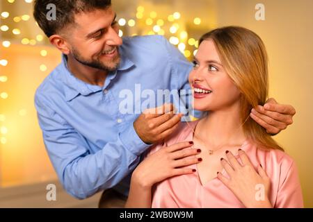 Homme donnant collier à la femme ravie avec des lumières brillantes en toile de fond Banque D'Images