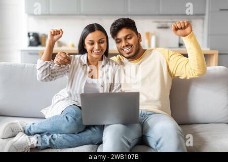 Portrait de Jeune couple indien joyeux célébrant le succès avec ordinateur portable à la maison Banque D'Images