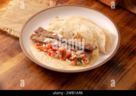 Tacos de Arrachera. Viande grillée maison dans une tortilla de blé. Cuisine de rue du Mexique, traditionnellement accompagnée de coriandre, oignon et sauce épicée Banque D'Images