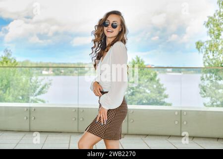 Portrait extérieur de jeune femme heureuse en chemisier et mini jupe avec motif pied d'oie Banque D'Images