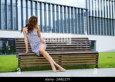 Femme méconnaissable avec de longues jambes minces en sandales sur banc Banque D'Images