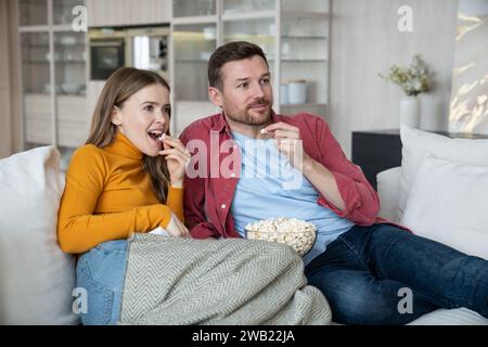 Amis couple regarder la télévision comédie drôle de film ensemble assis sur le canapé à la maison profiter de manger pop-corn. Banque D'Images