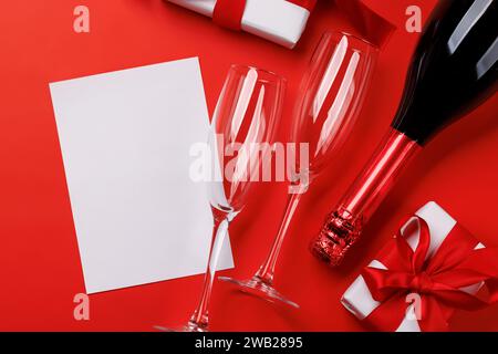 Champagne et cadeau : duo de célébration sur fond rouge avec espace texte. Carte de voeux pour la Saint-Valentin Banque D'Images