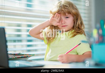 Fatigué triste garçon d'école en faisant des devoirs. Enfant tenir un crayon et dessiner à la maison. Un jeune garçon qui dessine à la table. Banque D'Images