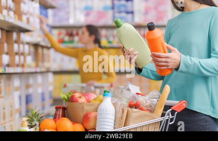 Femme achetant des produits à l'épicerie, elle compare deux bouteilles de détergents Banque D'Images