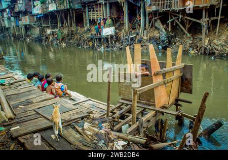 Indonésie, Jakarta. Enfant sur une toilette extérieure dans un bidonville. Banque D'Images