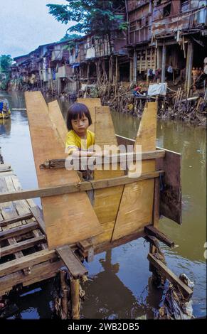 Indonésie, Jakarta. Enfant sur une toilette extérieure dans un bidonville. Banque D'Images