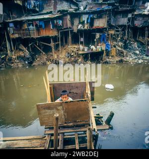 Indonésie, Jakarta. Enfant sur une toilette extérieure dans un bidonville. Banque D'Images