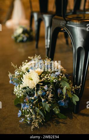 Arrangements floraux à côté de chaises noires sur l'allée de cérémonie de mariage Banque D'Images