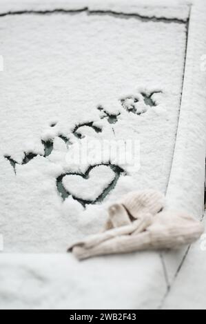 Les mots « hiver » et le symbole du cœur sont écrits dans la neige sur la vitre de la voiture Banque D'Images