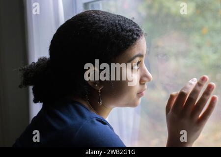 Biracial adolescente dans le profil regarde par une fenêtre Banque D'Images