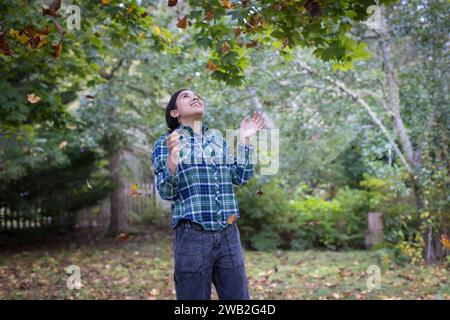 Adolescente biracial vomissant des feuilles d'automne et riant Banque D'Images