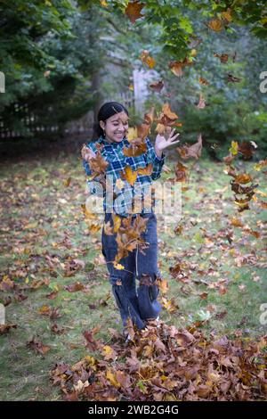 Adolescente biracial vomissant des feuilles d'automne et riant Banque D'Images