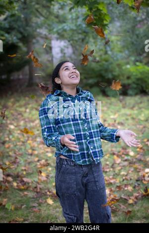 Adolescente biracial vomissant des feuilles d'automne et riant Banque D'Images