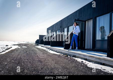 Une femme caucasienne debout sur le patio d'un bâtiment moderne donnant sur un chemin de terre dans la neige Banque D'Images