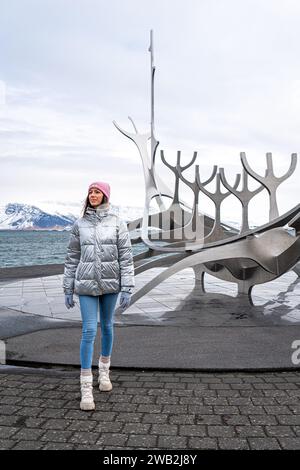Une jeune femme séduisante pose devant une sculpture moderne sur la plage Banque D'Images