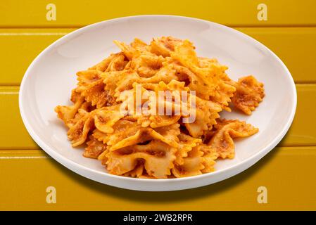Pâtes Farfalle avec sauce tomate et Chili et ail et huile d'olive dans une assiette blanche isolée sur table en bois jaune avec chemin de détourage inclus Banque D'Images