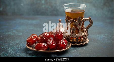 Rompre le jeûne avec des dattes séchées pendant le Ramadan Kareem, repas d'iftar avec des dattes et du thé arabe en verre traditionnel, vue d'angle sur fond bleu rustique Banque D'Images