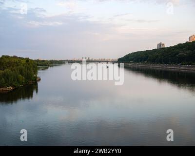 Vue du pont piéton du parc sur la rivière Dnipro au pont du métro, un bateau flottant et de grands bâtiments au loin à Kiev Banque D'Images