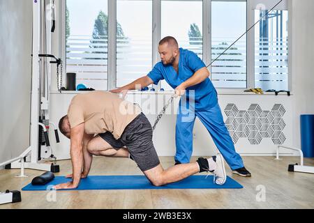 instructeur professionnel soutenant l'entraînement de l'homme pendant la séance de récupération dans la salle de gym du centre de kinésio Banque D'Images