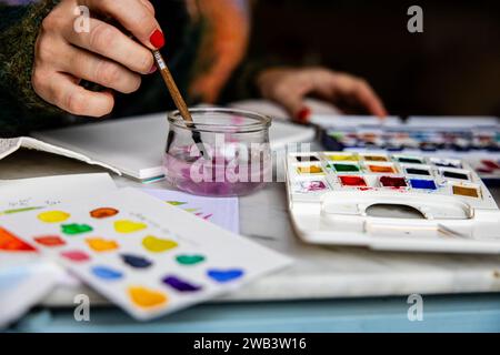 Détail des mains de la femme nettoyant la brosse à l'aquarelle dans l'eau avec des fournitures d'art. Banque D'Images