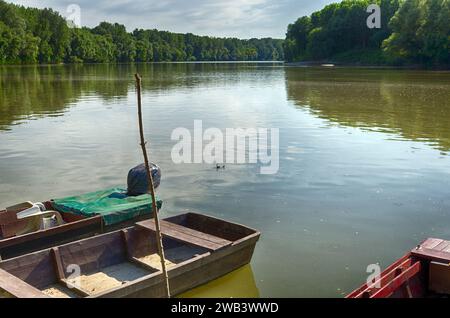 Hongrie, Tiszadada en été : les bateaux en bois reposent le long de la rive de la rivière Tisza, embrassés par les arbres, une scène pittoresque en été Banque D'Images