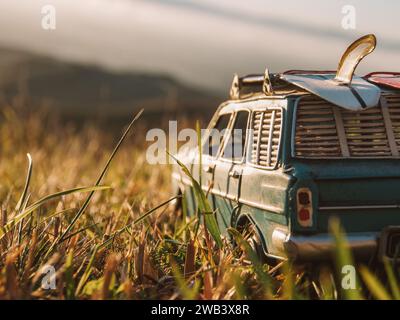 Voiture miniature vintage avec planche de surf sur le toit à l'extérieur au coucher du soleil. Banque D'Images