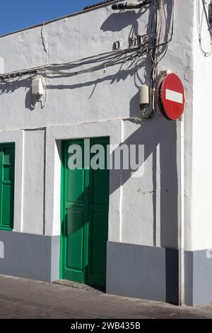 Coin d'un bâtiment bas, avec une façade blanche typique et porte verte et volet de fenêtre. De nombreux câbles au mur. Panneau de signalisation routière sans entrée. Bleu clair sk Banque D'Images