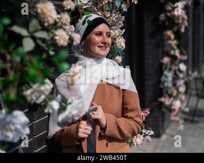 Portrait d'une jeune femme caucasienne vêtue d'un hijab près d'un mur avec des fleurs. Banque D'Images