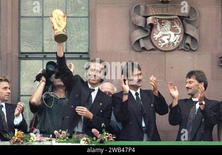 FILED - 09 juillet 1990, Hesse, FrankfurtMain : le Manager de l'équipe d'alors Franz Beckenbauer (l) tient le trophée de la coupe du monde qu'il a gagné en Italie sur le balcon de la Römer, riant. Il est flanqué de Raimond Aumann et Günther Hermann. Des milliers de personnes accueillent avec enthousiasme les joueurs de l'équipe allemande de coupe du monde de football sur le Römerberg. L'équipe nationale allemande de football est championne du monde pour la troisième fois. La veille, l’Argentine avait été battue 1:0 en finale à Rome. Franz Beckenbauer est mort. La légende du football allemand est morte dimanche à l'âge de 78 ans, sa famil Banque D'Images