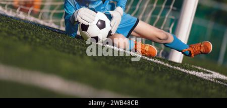 Jeune garçon comme gardien de but de football attraper le ballon pendant un match de football. Gardien de but de football en maillot et gants de sport jouent un tournoi de football Banque D'Images