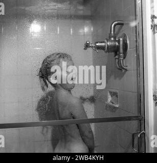 1991, jeune fille historique et excitée profitant de l'eau chaude d'une douche puissante, Angleterre, Royaume-Uni. Banque D'Images