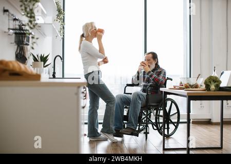 Retraité épouse et mari en fauteuil roulant buvant des boissons chaudes dans des tasses Banque D'Images