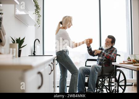 Retraité épouse et mari en fauteuil roulant buvant des boissons chaudes dans des tasses Banque D'Images