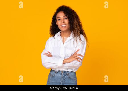 Jeune femme afro-américaine pose les mains croisées sur fond jaune Banque D'Images