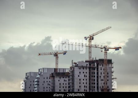 Trois grues tour au-dessus du projet d'immeuble d'appartements. Construction de condominiums. Coucher de soleil, heure dorée, noir et blanc, avec des nuages Banque D'Images