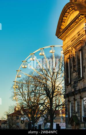 Coin de bâtiment historique avec une grande roue et des silhouettes d'arbres contre un ciel bleu clair au coucher du soleil à Lancaster. Banque D'Images