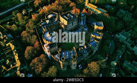 Vue aérienne d'un majestueux château de Lancaster entouré d'arbres luxuriants pendant l'heure d'or, mettant en valeur l'architecture historique et le paysage pittoresque. Banque D'Images