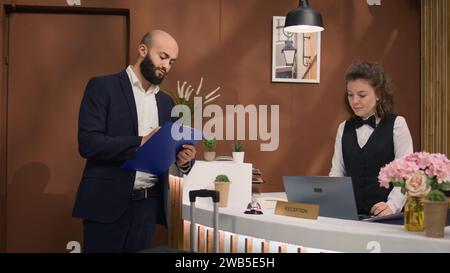 Cols blancs signant des papiers à la réception de l'hôtel, s'enregistrant avant de rencontrer des investisseurs internationaux. Homme d'affaires invité important voyageant pour le travail, signer des formulaires. Prise de vue à main levée. Banque D'Images