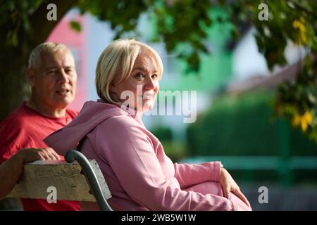 Couple âgé trouvant réconfort et joie alors qu'ils se reposent sur un banc de parc, engagés dans une conversation sincère, après un strol rajeunissant dont un témoignage Banque D'Images