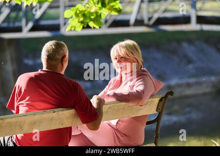 Couple âgé trouvant réconfort et joie alors qu'ils se reposent sur un banc de parc, engagés dans une conversation sincère, après un strol rajeunissant dont un témoignage Banque D'Images