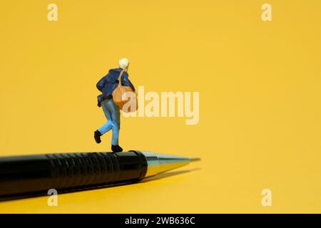 Photographie miniature de figurine de jouet de personnes minuscules. Un étudiant courant au-dessus d'un sac de transport de crayons. Isolé sur fond jaune. Image photo Banque D'Images