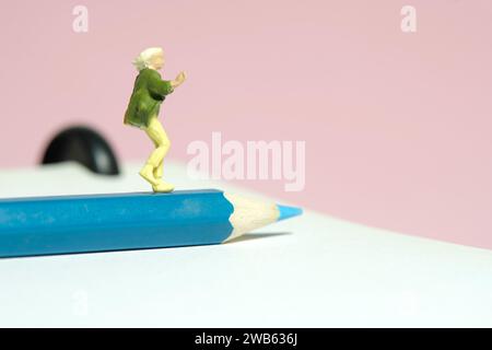 Photographie miniature de figurine de jouet de personnes minuscules. Un étudiant courant au-dessus d'un sac de transport de crayons. Isolé sur fond rose. Image photo Banque D'Images