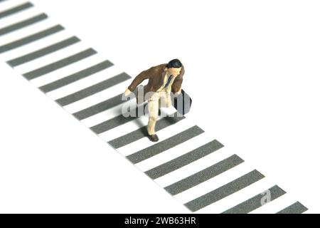 Photographie miniature de figurine de jouet de personnes minuscules. Un homme d'affaires portant un manteau marchant seul sur un passage de zèbre à la rue. Isolé sur fond blanc Banque D'Images