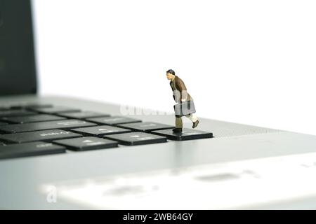 Photographie miniature de figurine de jouet de personnes minuscules. Un homme d'affaires courant au-dessus du clavier ordinateur portable portant une mallette. Isolé sur fond blanc. I. Banque D'Images