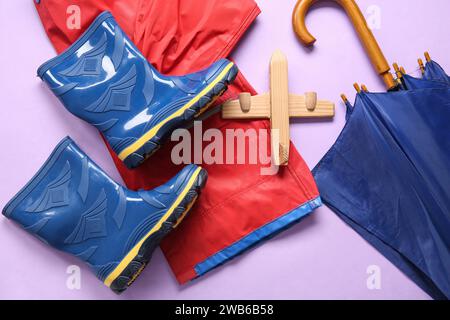 Bottes en gomme bleue avec veste, parapluie et avion jouet sur fond lilas Banque D'Images