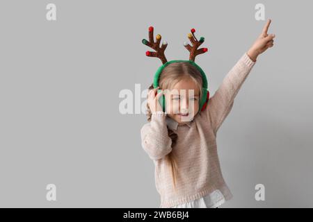 Jeune fille heureuse dans les bois de renne et les cache-oreilles pointant vers quelque chose sur fond gris Banque D'Images