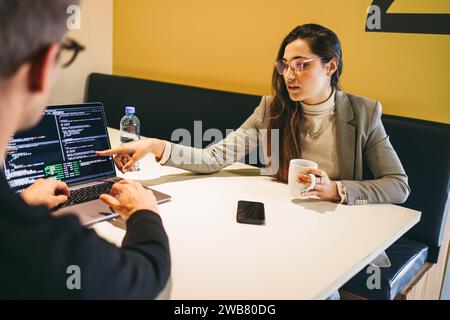 Les professionnels du codage, un homme et une femme, codent et collaborent dans un bureau moderne. Ils discutent de la conception de logiciels, mettant en valeur le travail d'équipe et l'expertise. TH Banque D'Images