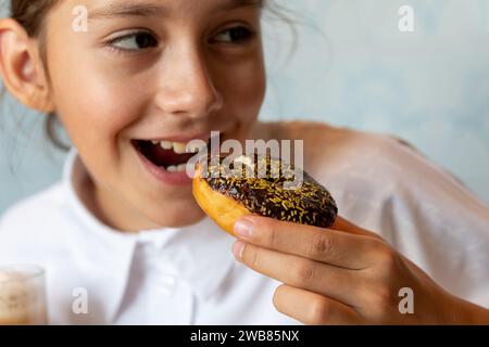 Fille mangeant du Donut sucré. Fille mangeant du gâteau en hiver, Portrait de belle fille avec beignet chocolat. Banque D'Images