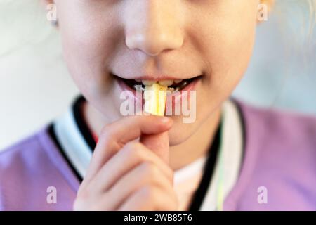 L'enfant mange des frites joyeusement. petite fille ouvre la bouche pour manger une tranche de pommes de terre. Portrait d'enfant dans un café fast-food. Banque D'Images